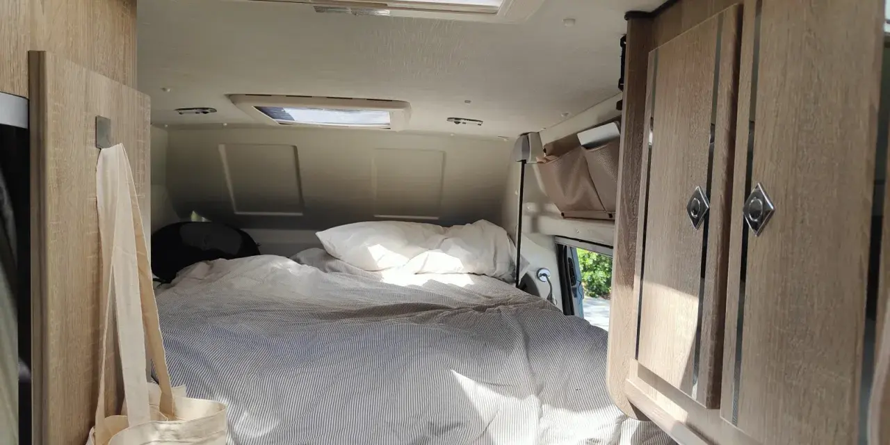 Mysig säng med randigt täcke i en Karmann Mobil. En tygkasse hänger på en krok.