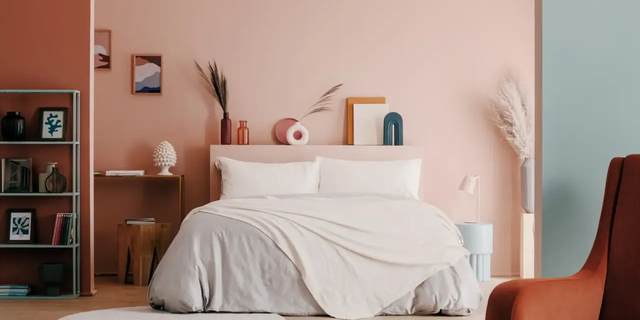 Camera da letto moderna con letto king-size, biancheria grigia e coperta color crema. Idee per come abbellire una camera da letto con decorazioni astratte e piante.