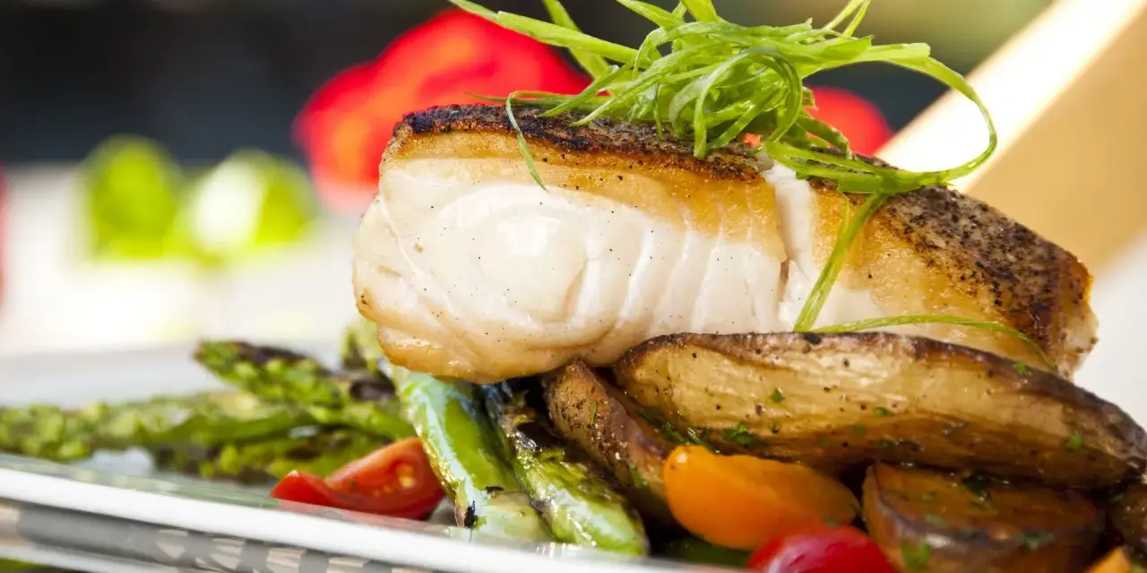 Aromatyczny halibut na talerzu z pieczonymi ziemniakami, szparagami i pomidorkami. Zapach halibut na jakie ryby?