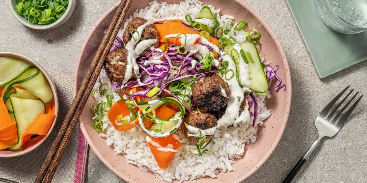 En skål med ris, köttbullar, strimlad rödkål, morötter och gurka, toppad med en krämig sås. En härlig vietnamesisk matupplevelse.