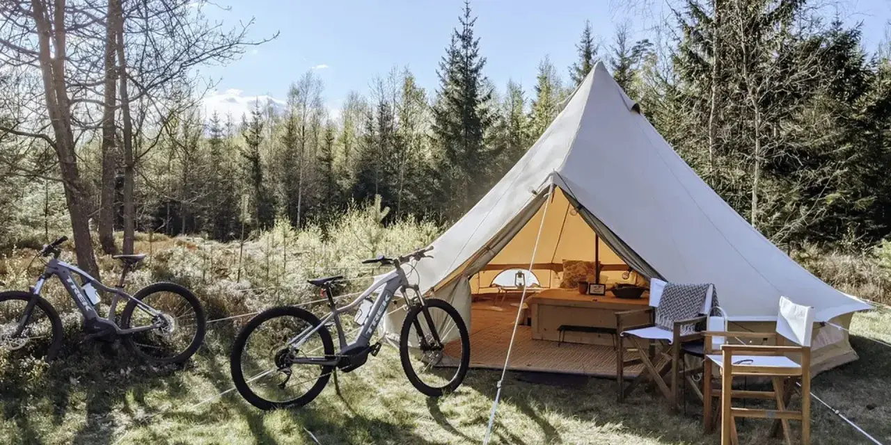 Två elcyklar står redo för äventyr vid ett stort tält på Bengts camping. Skogen bakom bjuder in till utforskning.