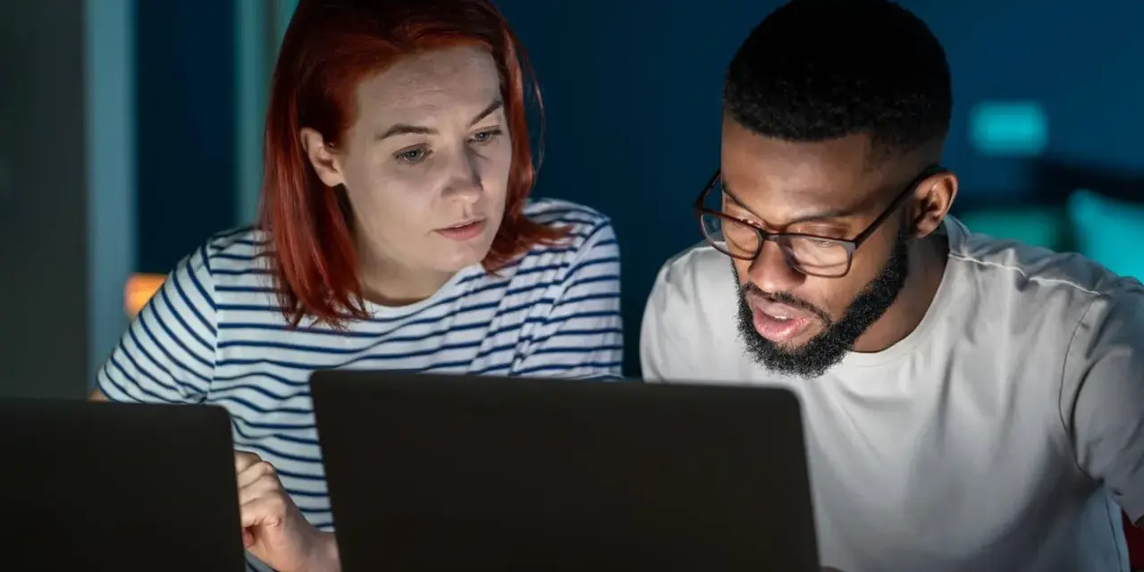 Zwei Personen arbeiten konzentriert an Laptops. Sie besprechen Details, vielleicht für einen partnerschaftsvertrag ohne notar.