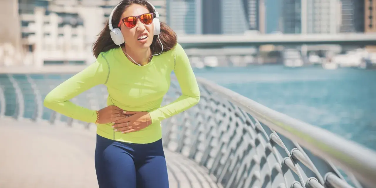 Une coureuse en tenue de sport, écouteurs aux oreilles, se tient le ventre, visiblement prise d'un point de côté.