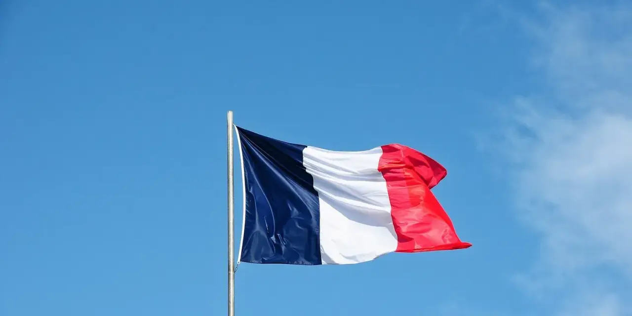 Die französische Flagge weht im Wind vor blauem Himmel. Ein Symbol für ein spannendes Auslandsjahr in Frankreich.