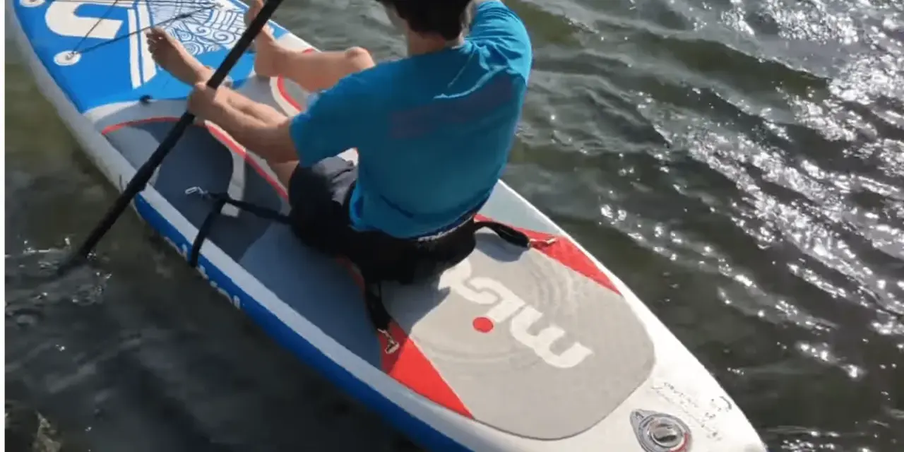 Mann sitzt auf SUP-Board, paddelt und befestigt den Sitz.