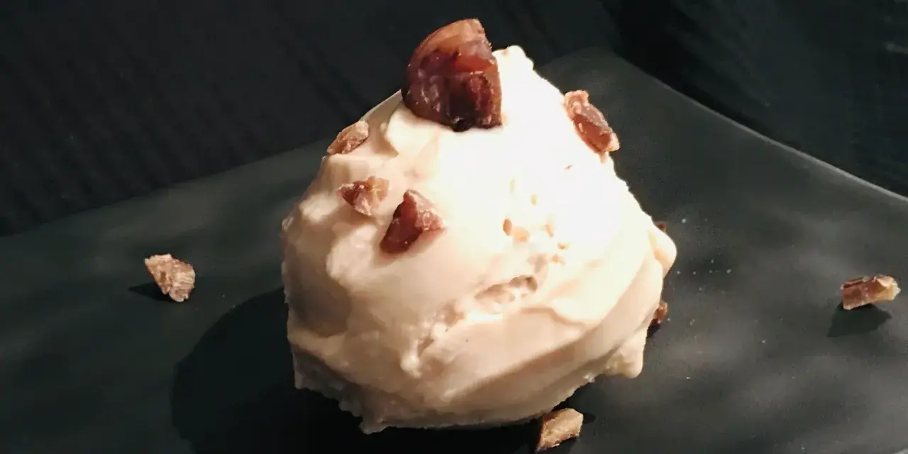 Cremiges Maronen Eis, garniert mit kleinen Maronenstückchen, auf einem dunklen Teller. Ein Genuss für kalte Tage.