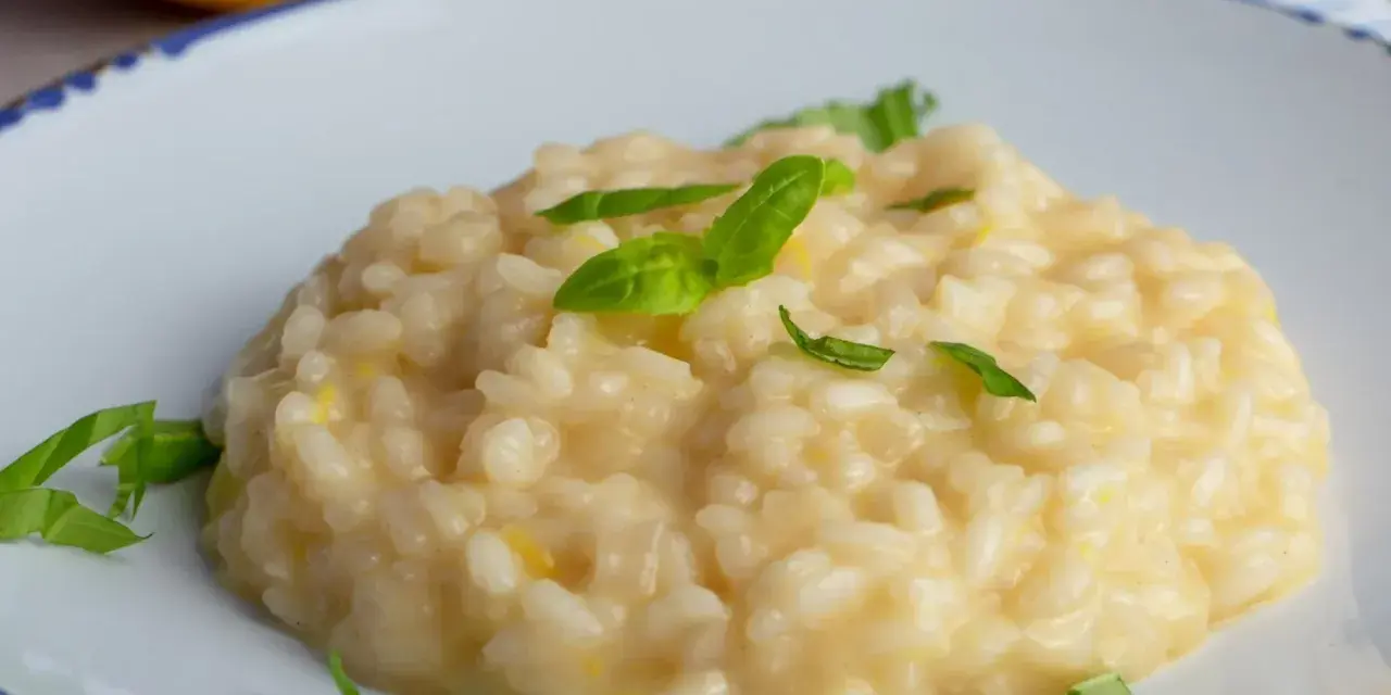 Kremowe, letnie risotto z cytryną i bazylią, podane na białym talerzu z niebieskim rantem.