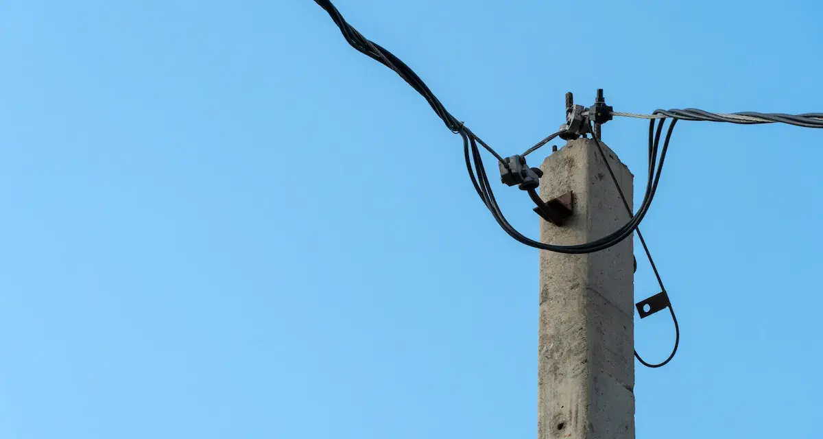 Betonowy słup energetyczny z przewodami na tle błękitnego nieba. Zastanawiasz się, ile za słup energetyczny na działce?