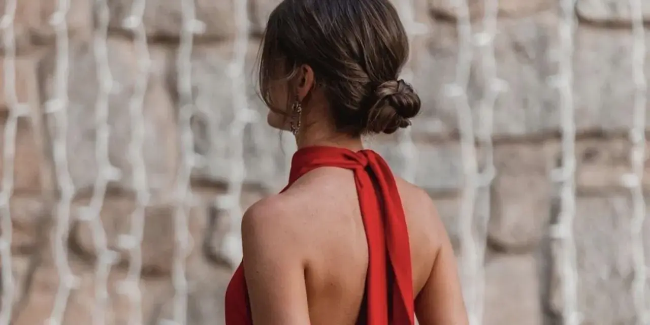 Elegante moño bajo en una mujer con vestido rojo, luciendo su espalda descubierta y un pendiente llamativo.
