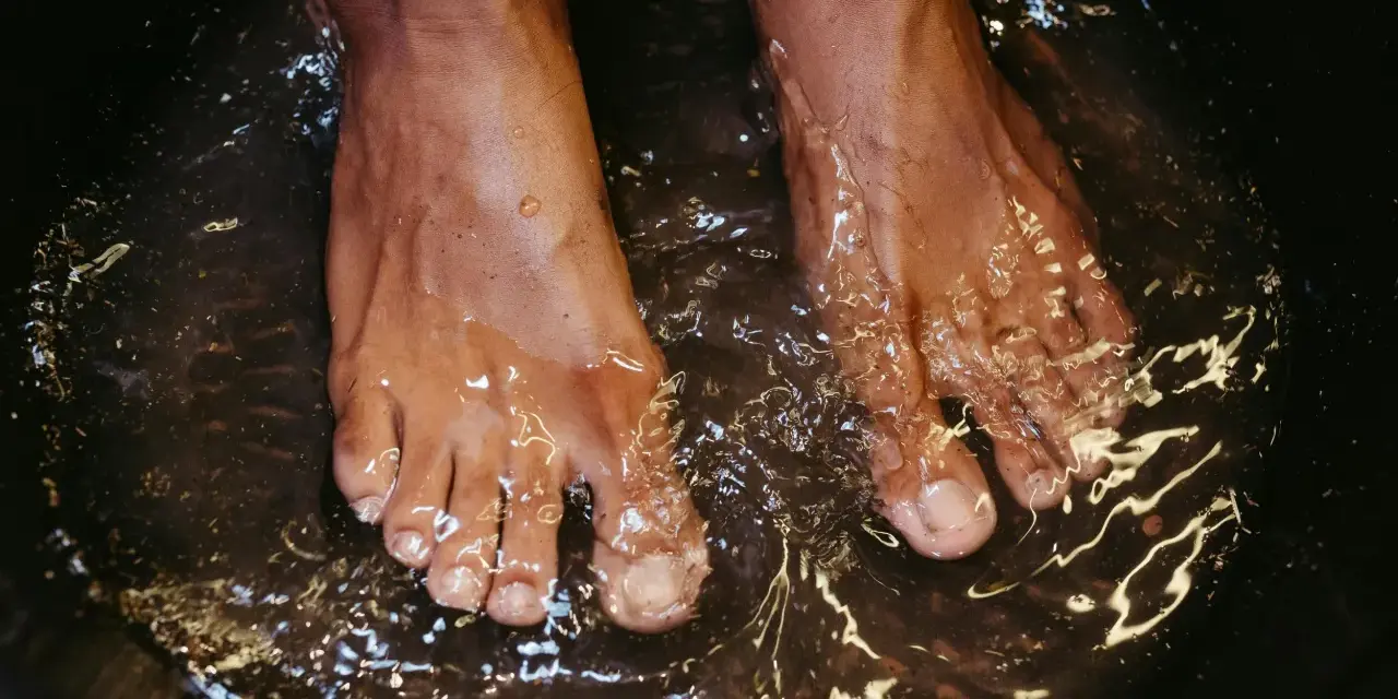 A close-up of feet soaking in a dark basin, likely a relaxing foot bath with epsom salt for feet.
