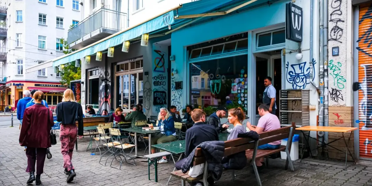 Menschen sitzen an Tischen vor einem **Prenzlauer Berg Restaurant** mit türkisfarbener Markise und Graffiti.