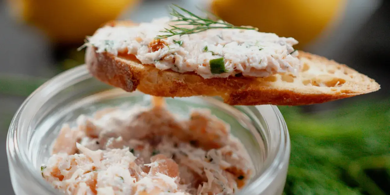 Un toast garni de rillettes de saumon, décoré d'aneth, avec un pot de rillettes en arrière-plan.