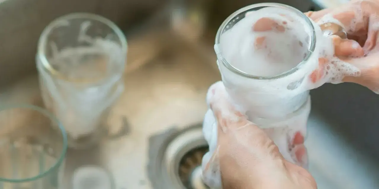 Händer tvättar ett glas med skum. Kanske med hjälp av Aquapel för en renare diskning.