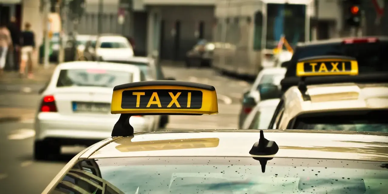 Ein Taxi mit leuchtendem "TAXI"-Schild auf dem Dach, bereit für Fahrten, auch im nachttarif. Regentropfen auf der Windschutzscheibe.
