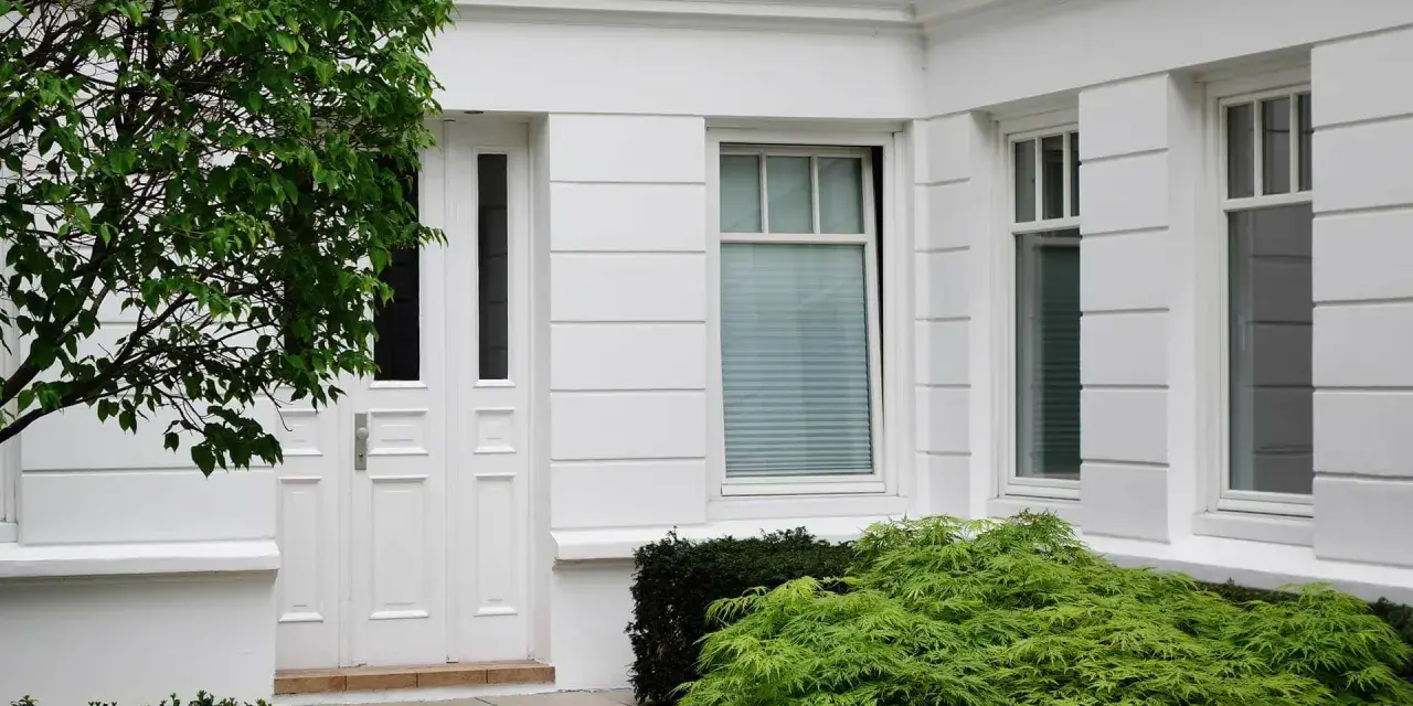 Boniowanie elewacji domu podkreśla jego klasyczny charakter. Białe drzwi i okna, otoczone zielenią, tworzą elegancką całość.