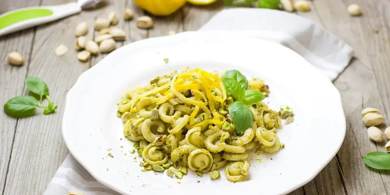 Makaron z zielonym pesto, którego głównym składnikiem są pistacje, ozdobiony skórką cytrynową i listkami bazylii.