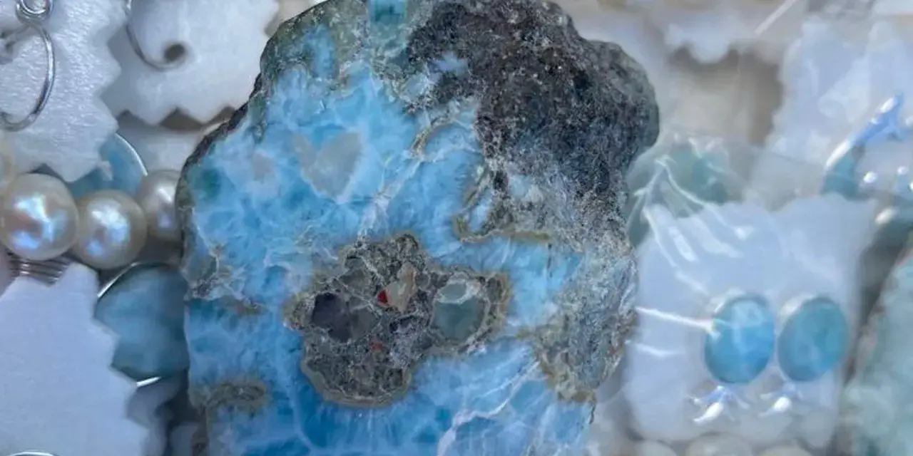 Surowy larimar, kamień o niebiesko-białych żyłkach, otoczony perłami i ozdobami. Jego magiczne właściwości uspokajają i przynoszą harmonię.