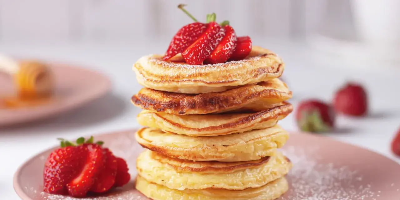Pancakes dorati, perfetti per una ricetta pancake veloce senza lievito, guarniti con fragole fresche e zucchero a velo.