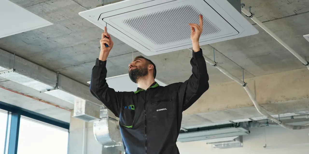 Técnico ajustando una unidad de cassette para la instalación de ventilación en un techo de hormigón.