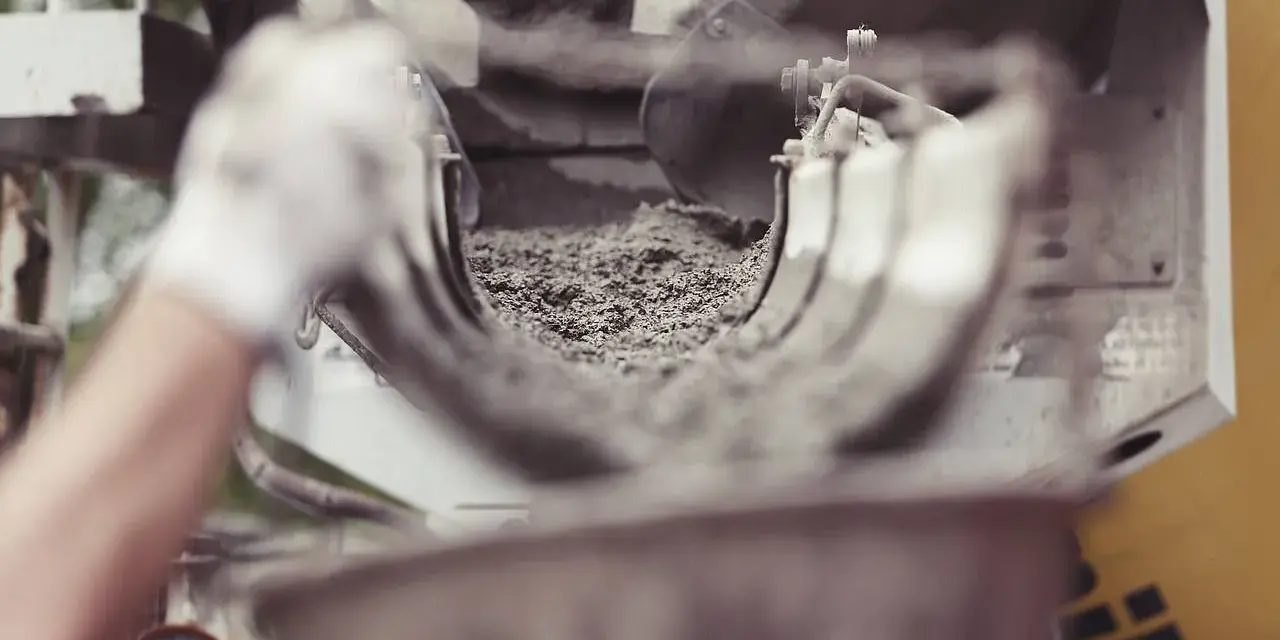 Ręka w rękawiczce kieruje strumień cementu do maszyny. Zastanawiasz się, ile kosztuje worek cementu?