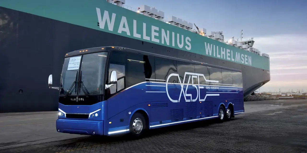 Niebieski autokar Van Hool CX45 z napisem "ZERO EMISSIONS" stoi przy ogromnym statku Wallenius Wilhelmsen.