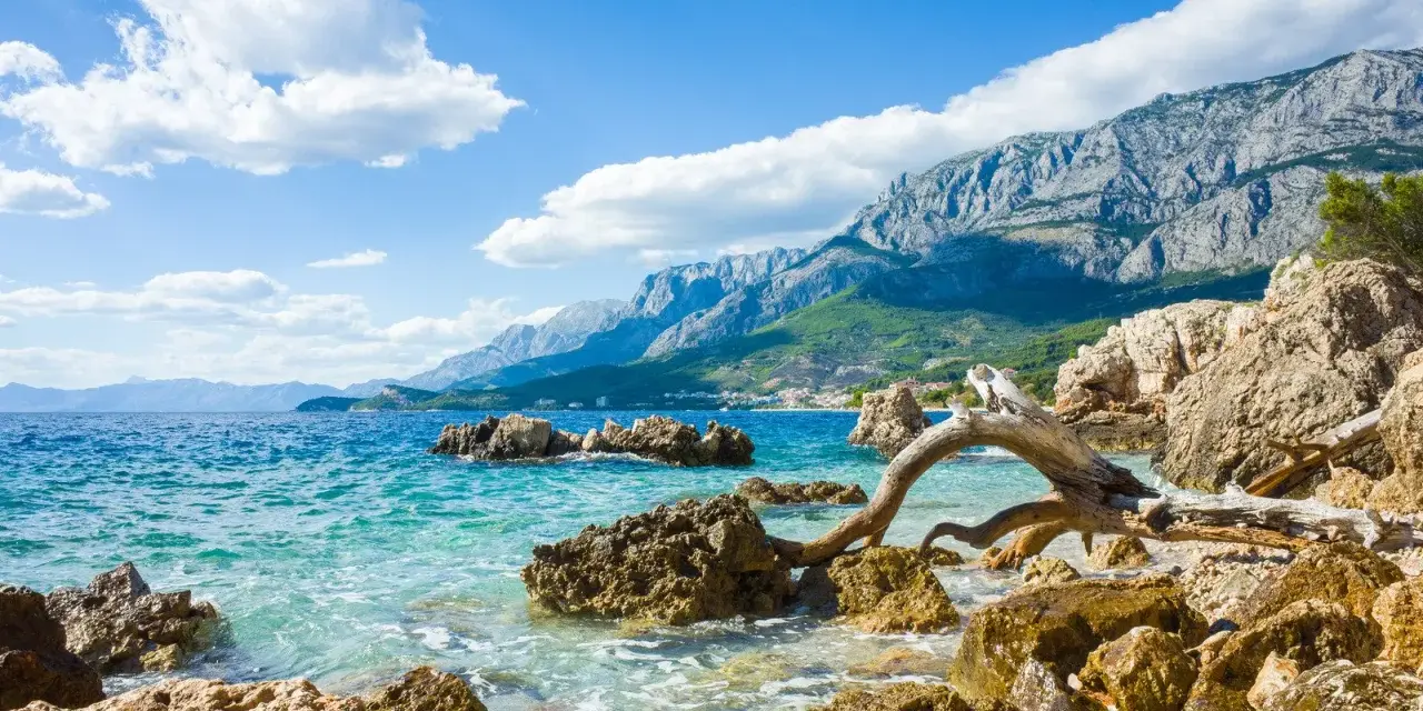 Piękne wybrzeże Chorwacji z turkusową wodą, skalistą plażą i górzystym krajobrazem w tle. Idealne miejsce, by zastanowić się, gdzie do Chorwacji.
