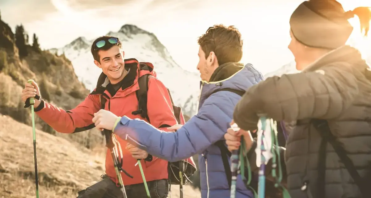 Trois randonneurs souriants, prêts pour une reconversion accompagnateur moyenne montagne, profitent du soleil couchant sur les sentiers.