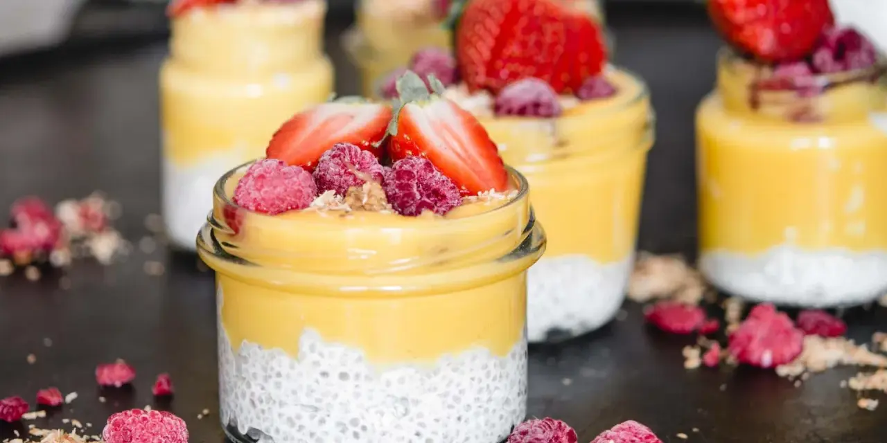 Erfrischender Mango Chia Pudding in Gläsern, garniert mit Erdbeeren und Himbeeren. Ein gesunder Genuss!