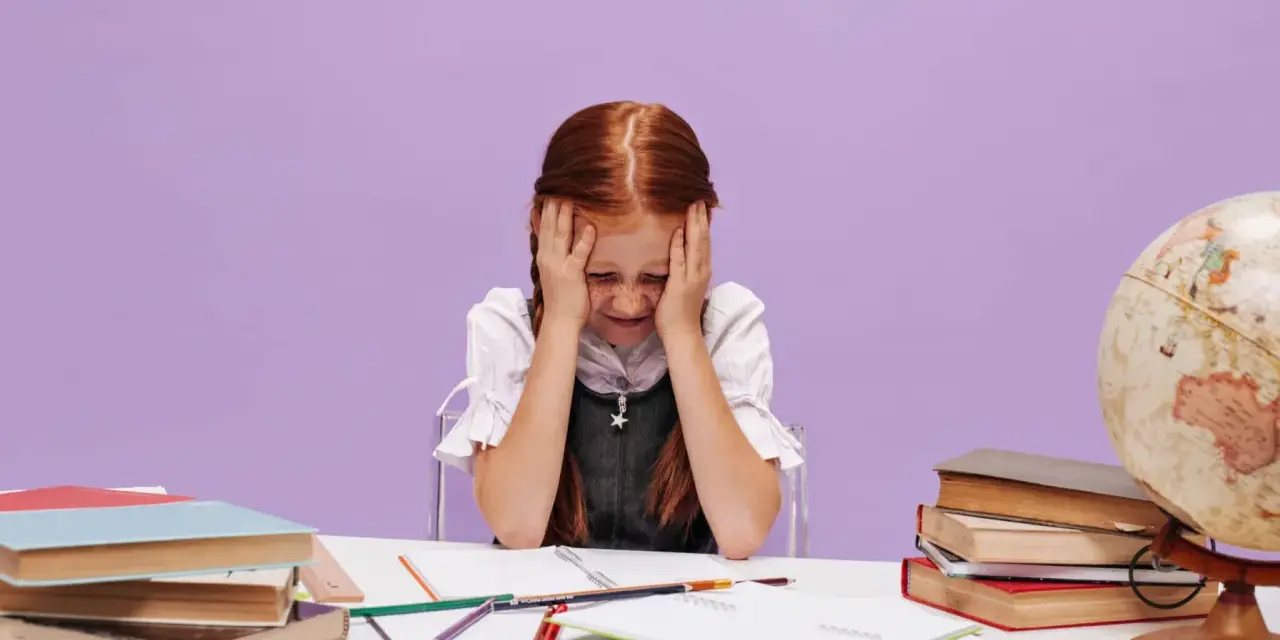 Une petite fille rousse, les mains sur la tête, semble dépassée par ses devoirs. La scène évoque les défis de la réglementation du dortoir maternelle.