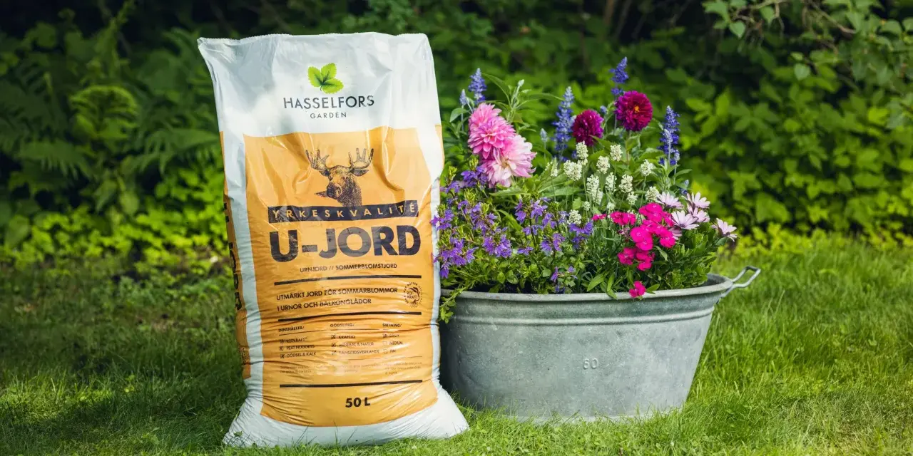 En säck U-jord från Hasselfors Garden står bredvid en zinkbalja fylld med färgglada blommor, redo att plantera.