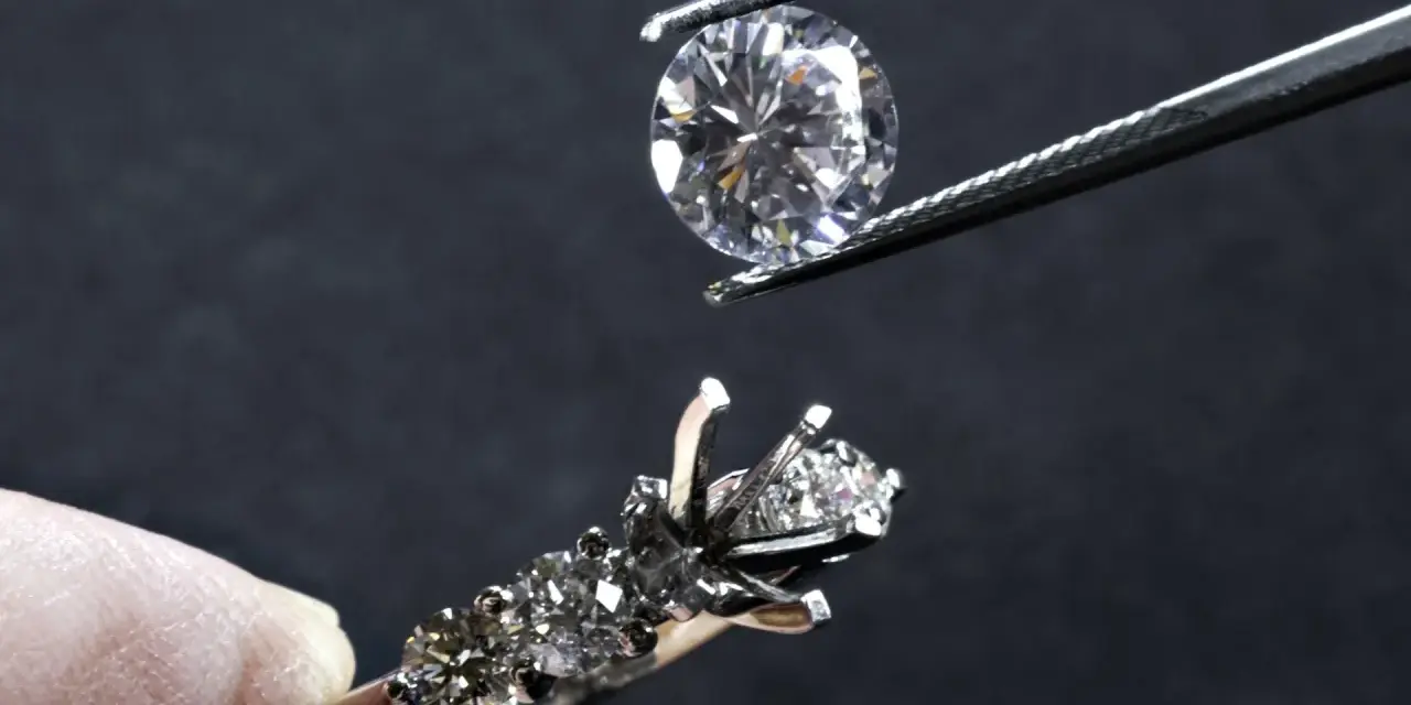Un diamante viene posizionato con una pinzetta su un anello con incastonatura a castone ribattuto, pronto per essere fissato.