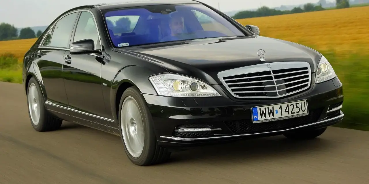 Czarny Mercedes-Benz W221 pędzi po drodze, mijając pola.