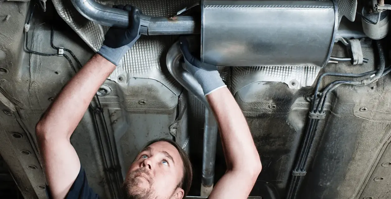 Mechanic working on a car's exhaust system. This tune up consists of replacing a section of the exhaust pipe and muffler.