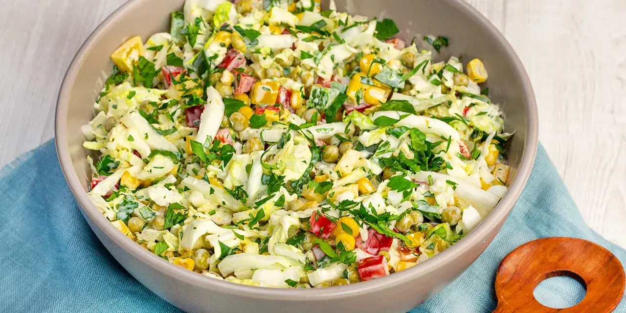 Schüssel mit knackigem Salat aus Weißkohl, Mais, Erbsen und Paprika, perfekt als salate zum vorbereiten am vortag. Mit frischer Petersilie garniert.