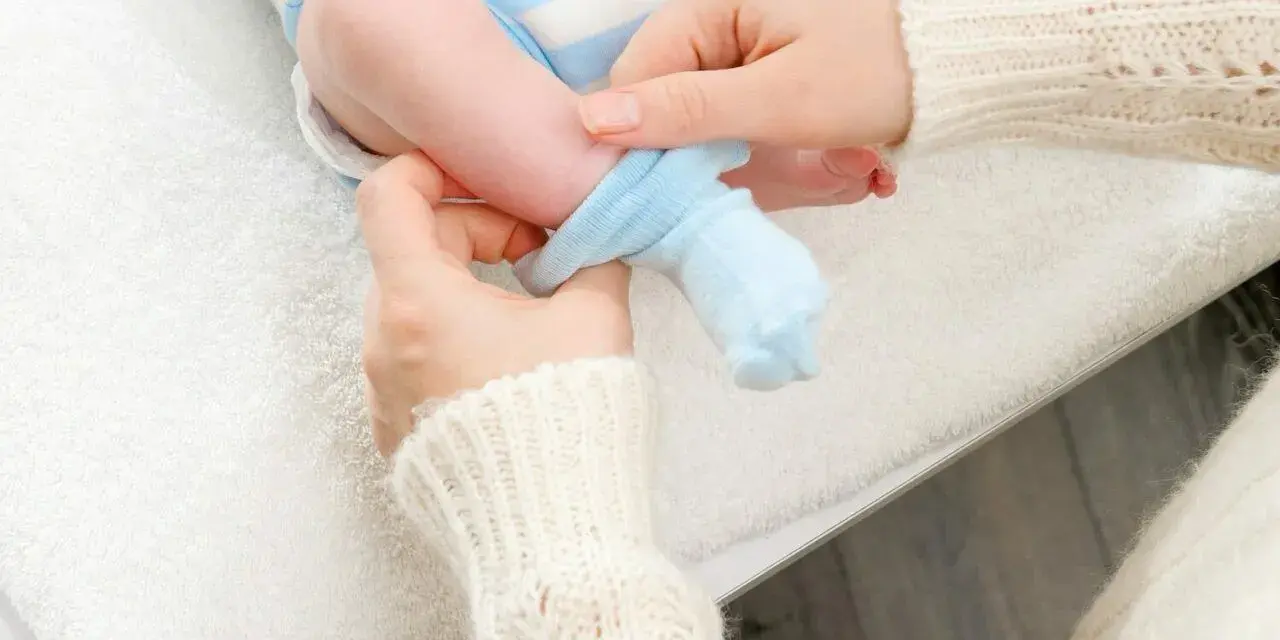 Mama zakłada niebieskie skarpetki na nóżki noworodka. Dobieranie odpowiedni jaki rozmiar skarpetek dla noworodka jest ważne.
