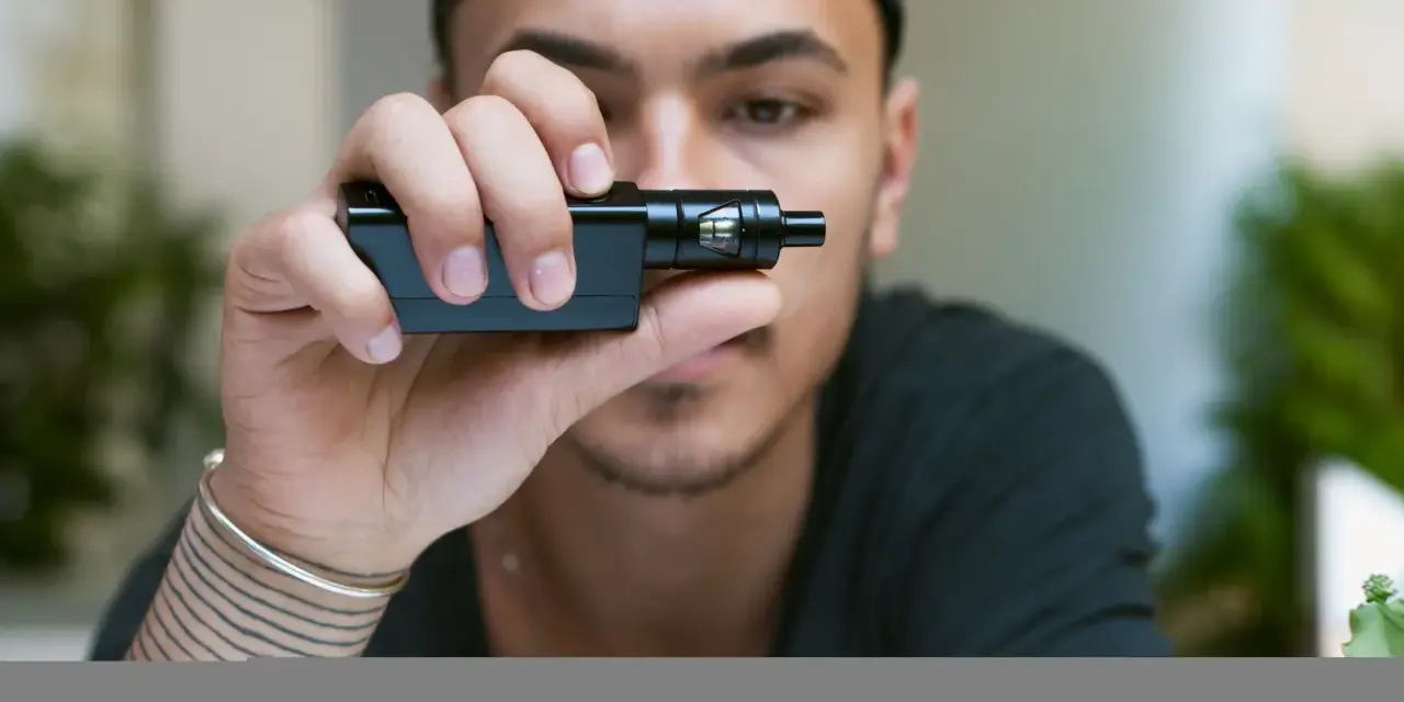 Joven con gorra negra sostiene un cigarrillo electrónico, mostrando sus claromizadores.