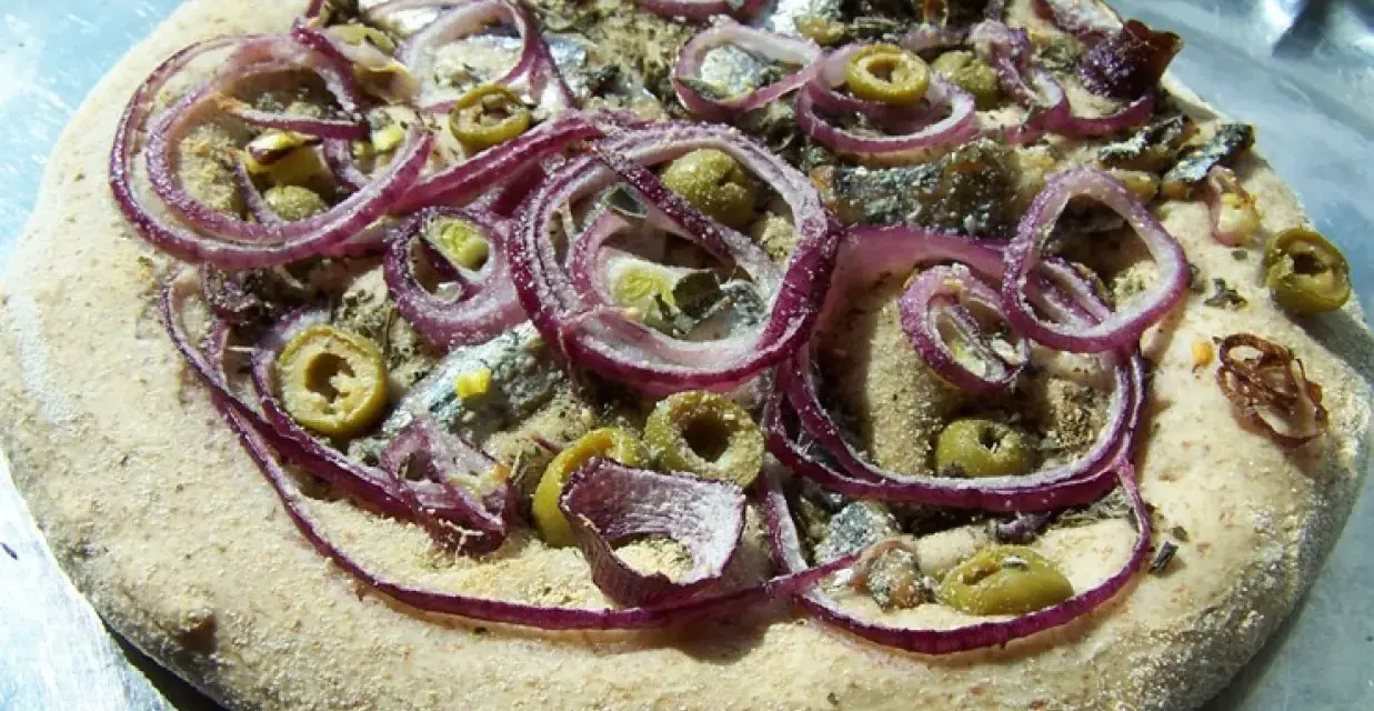 Pizza z anszua, oliwkami i czerwoną cebulą, gotowa do pieczenia.