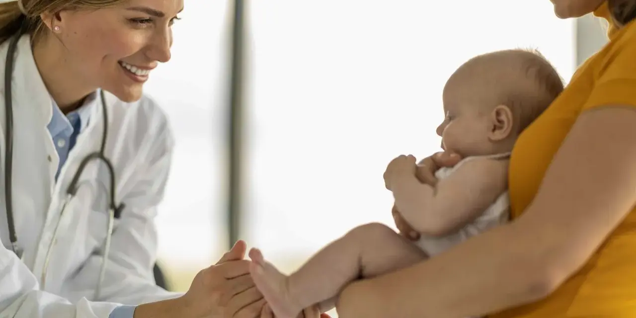 Lekarka bada niemowlę, które może być narażone na adenowirusa u dzieci. Uśmiechnięta lekarka delikatnie dotyka stópki dziecka.