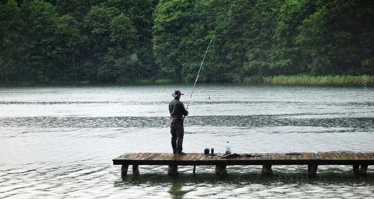 Ein Angler steht auf einem Steg und übt aus, wie angelt man, während es regnet.