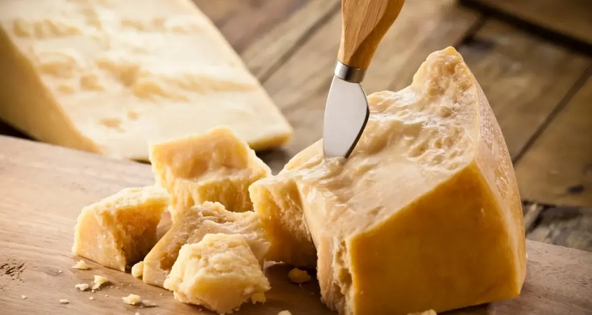Kawałki Grana Padano i parmezanu na drewnianej desce. Nóż wbity w duży kawałek sera.