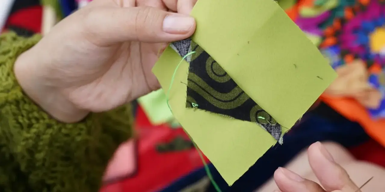 Ręce szyją zielone kwadraty z czarnym wzorem, tworząc patchwork projekty.