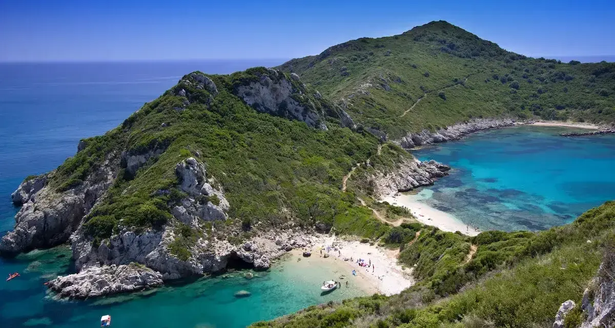 Malownicza zatoka z turkusową wodą i piaszczystą plażą, otoczona zielonymi wzgórzami. Tak właśnie wygląda Korfu, grecka wyspa, gdzie leży ten raj.