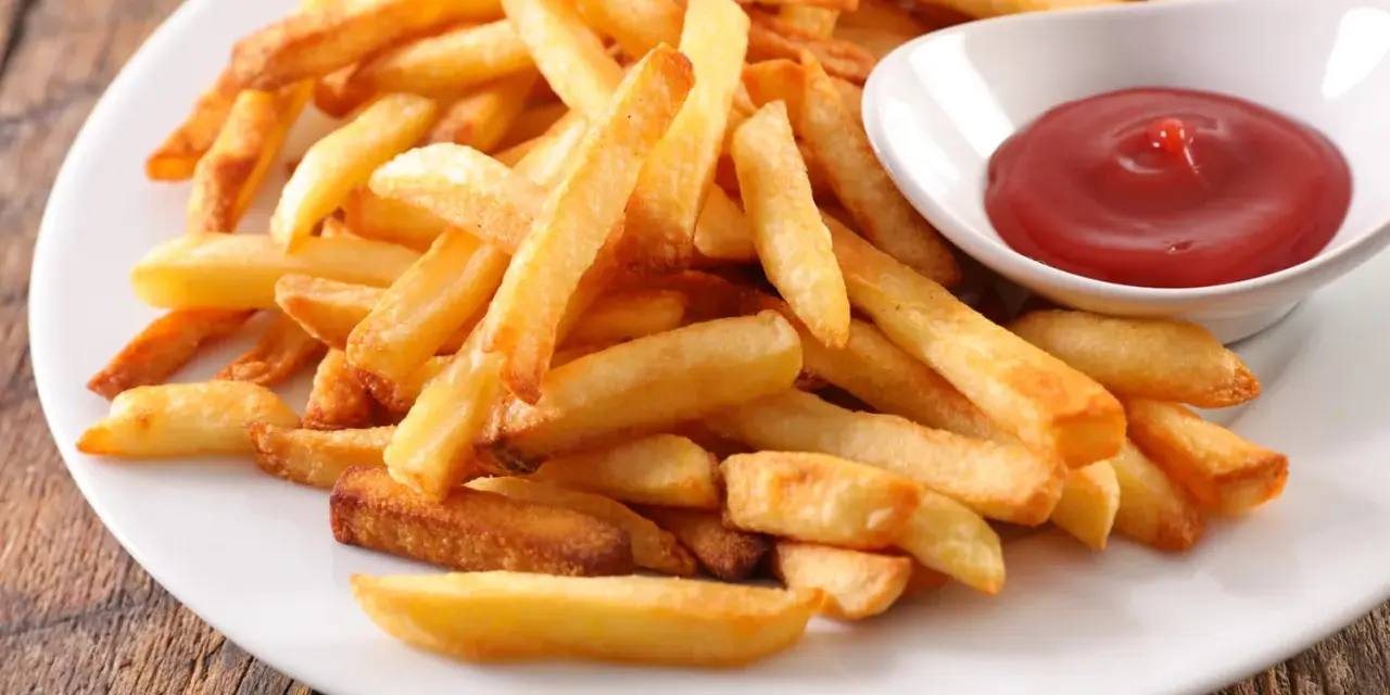 Une assiette de frites au four dorées et croustillantes, accompagnées d'un petit bol de ketchup rouge vif.