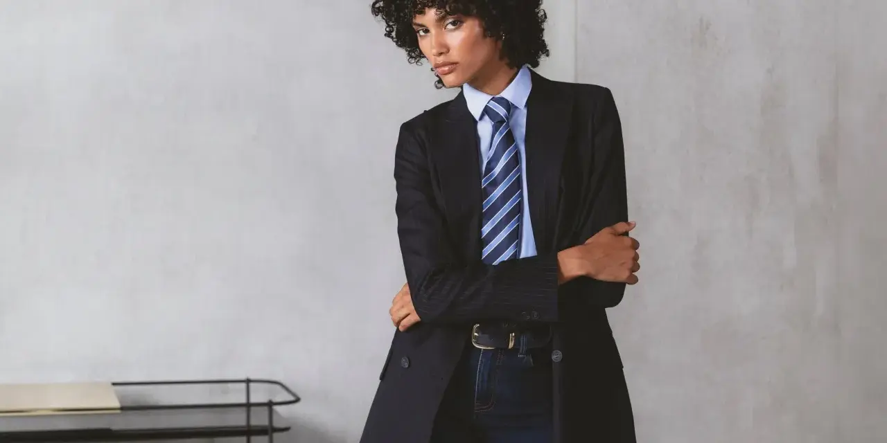 Persona androgina con traje a rayas, camisa azul y corbata a juego, posando con confianza.