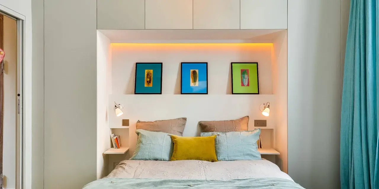 Idee salvaspazio camera da letto piccola: letto con testiera contenitore, quadri colorati e tende turchesi creano un ambiente accogliente.