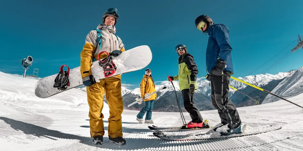 Grupa przyjaciół cieszy się jazdą na nartach i snowboardzie w marcu. Słońce świeci, a śnieg jest idealny do zjazdów.