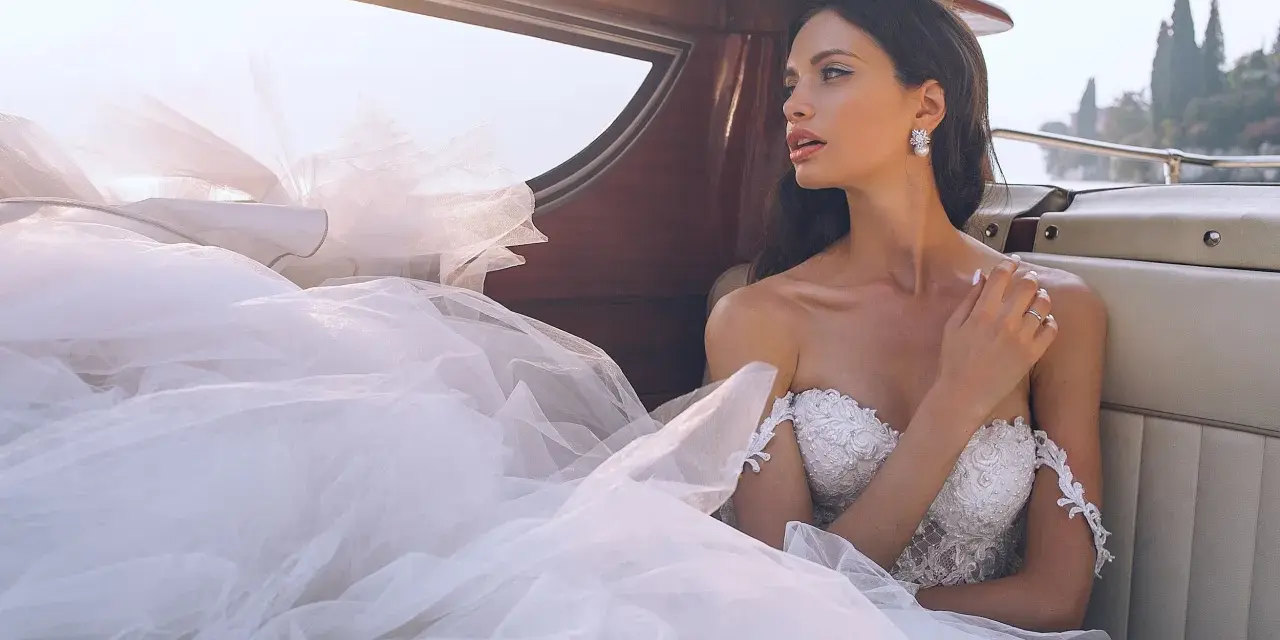 Sposa con abito bianco e trucco impeccabile, seduta su una barca, con il velo che ondeggia al vento.