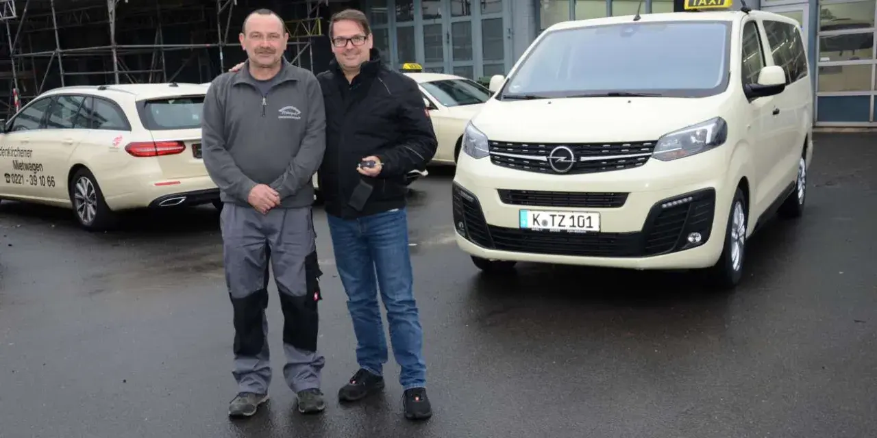 Zwei Männer stehen vor einem gelben Taxi und einem Kombi. Die Taxifahrt und der Steuersatz sind wichtige Themen für sie.