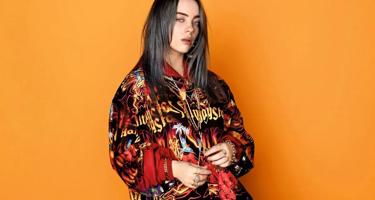 Billie Eilish w kolorowej bluzie, z mnóstwem złotych łańcuchów i pierścionków, jakby przygotowywała się do odebrania kolejnych nagród.