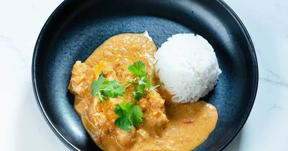 En krämig butter chicken med ris och färsk koriander i en svart skål.